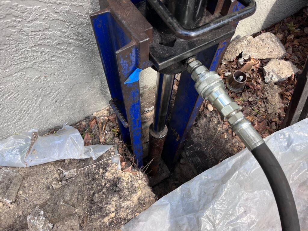 Close-up of Sinkhole Titan blue steel bracket and hydraulic pier system next to a stucco wall